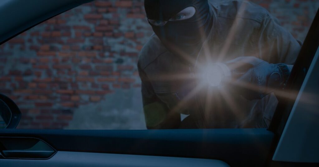 Thief wearing balaclava, holding a torch, looking into a car