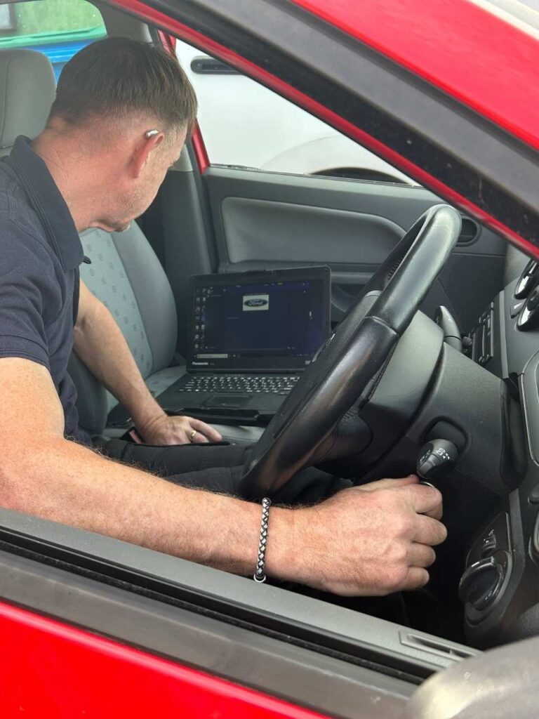 locksmith using a laptop inside of a car to programme a key